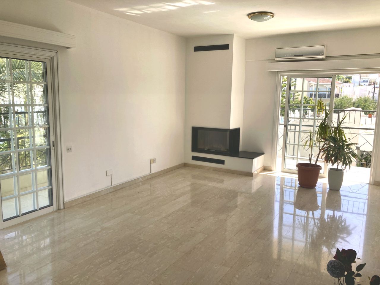 Bright, recently renovated living room with a modern corner fireplace and balcony doors in the Engomi apartment